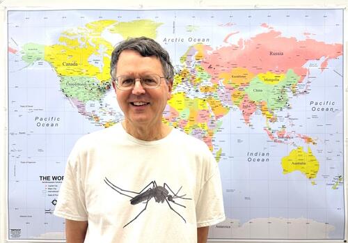 John Carlson, standing in front of a map. The pins on the map represent where his lab members have come from. 