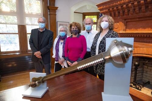 A group of people stand next to a table. The FAS Mace sits on the table.