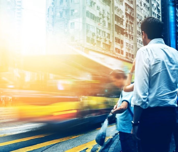 People stand in front of a street as a bus passes. Image credit: Adobe Stock