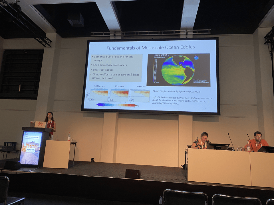 Yankovsky presents her research. She stands in front of a presentation slide titled "Fundamentals of Mesoscale Eddies."