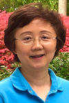 Headshot of Hui Cao, standing in front of pink flowers and smiling. 