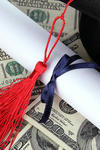 Stock image of a college diploma lying atop dollar bills 