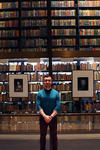 Portrait of Alexander, standing in front of book shelves at Beinecke Library. 